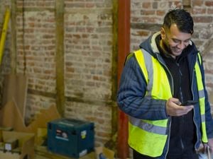 A tradesperson in a high-vis vest looking at his phone on a construction site.