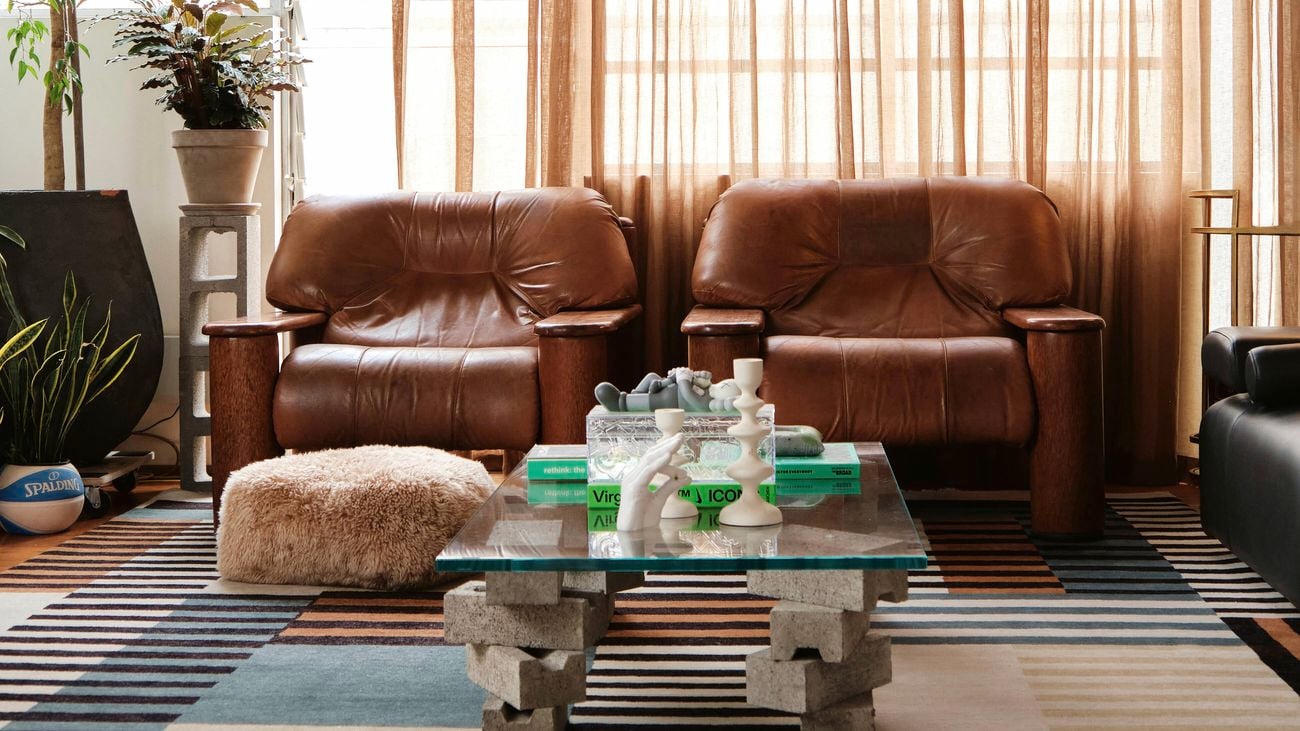 Living room with two brown leather armchairs, a glass and concrete block coffee table, a striped rug and paper lanterns