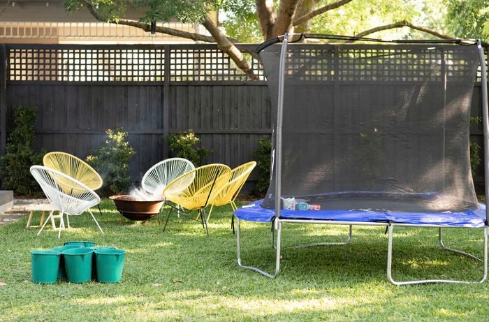 Backyard with a trampoline and chairs set around a firepit.
