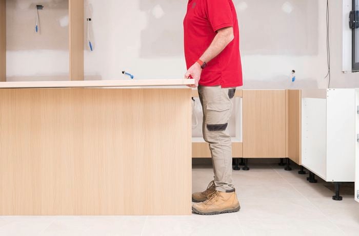 A Bunnings Team Member is positioning the benchtop on the cabinets to check how it sits.