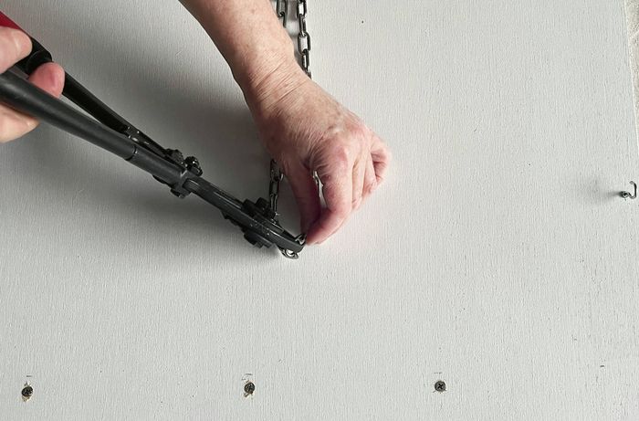 Hands using bolt cutters to cut a chain in front of a white-painted plywood panel. [[2609] MAK...me sign_V1 | Word]