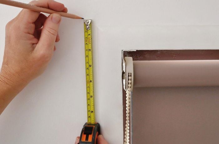A pair of hands marking a window frame to install curtain brackets