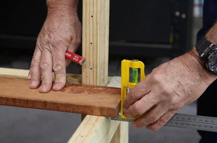Person measuring wooden garden bench frame pieces.