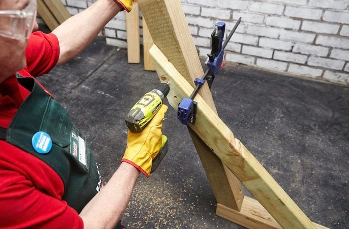 Person drilling two pieces of timber together that are being held by clamp.