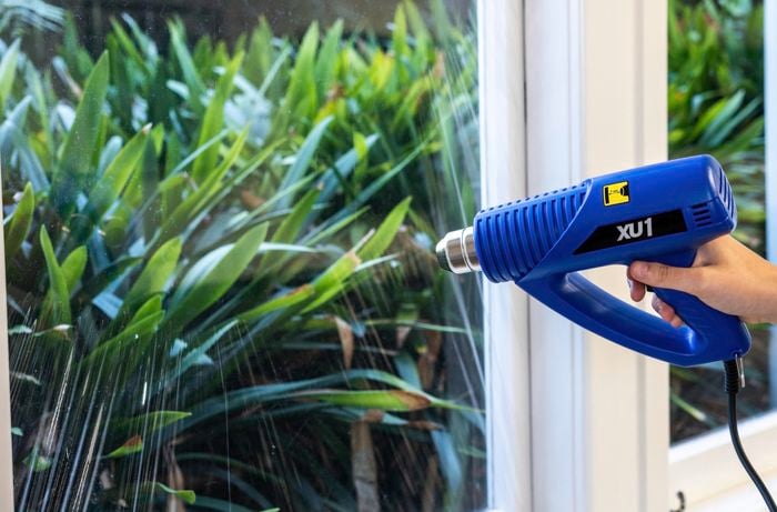 A person holding a heat gun against a window