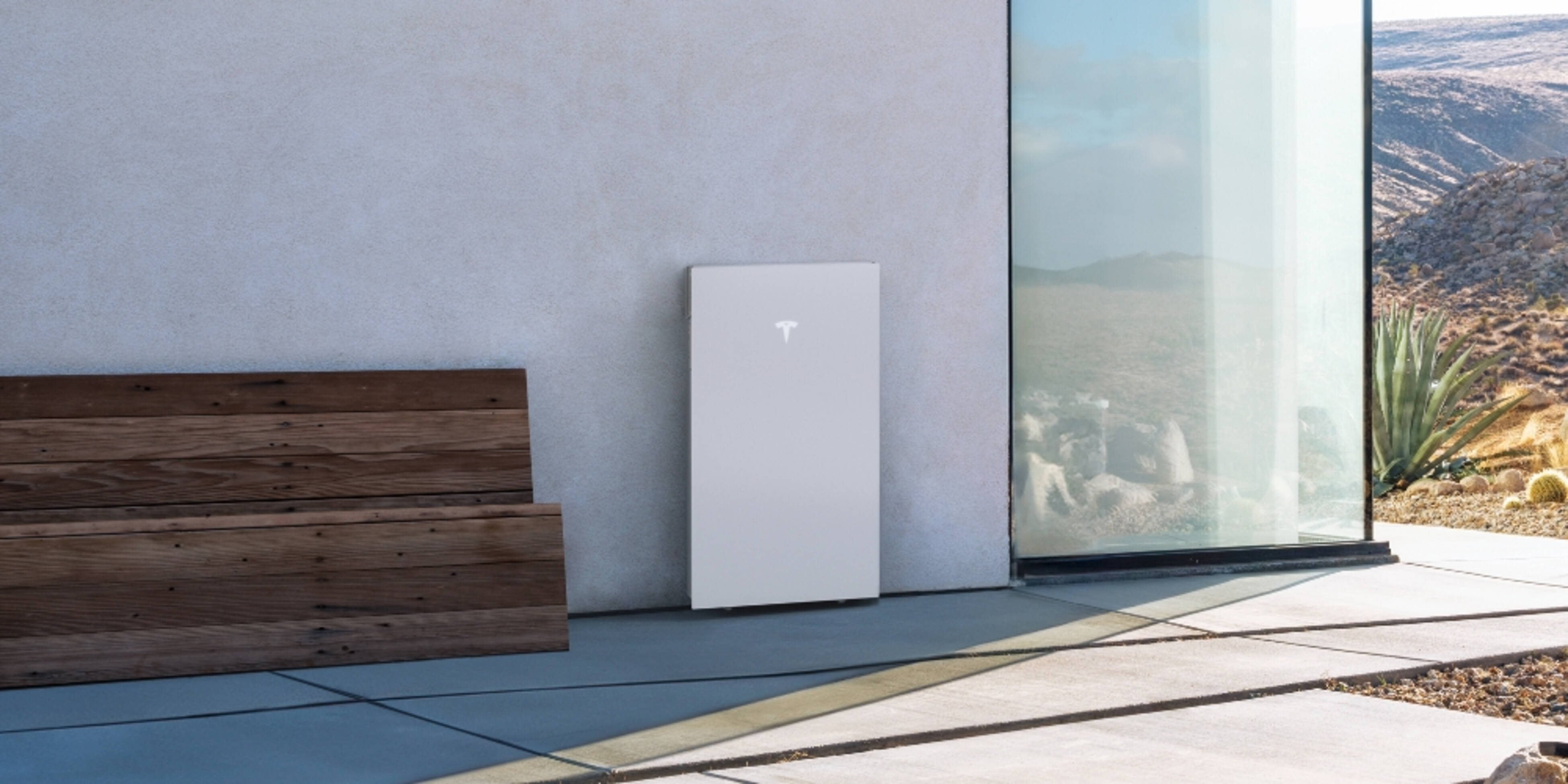 A Tesla Powerwall 3, rectangular in shape and white in colour, cleanly installed on a garage wall of a home, mounted above the ground and with cabinetry alongside.