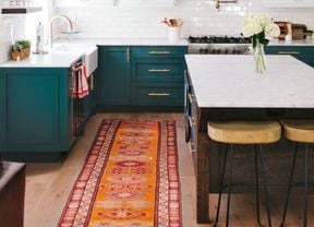 A kitchen with dark green cabinets and white benchtops and tiles
