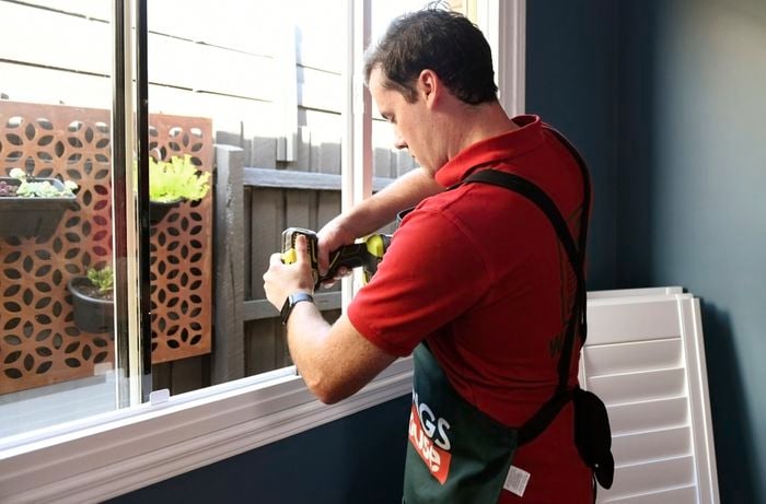 Person using cordless drill to attach plantation shutter frame to window frame