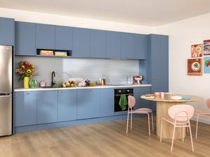 Blue modern kitchen, with items on the benchtop, a fridge and table and chairs in it.