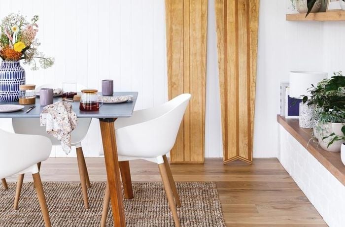 Dining room with white chairs, timber bench seat and plants.