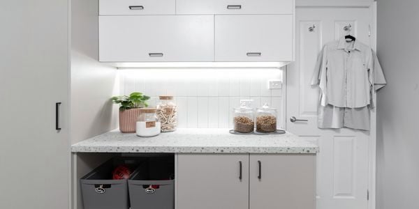 Laundry with grey cabinets, marble benchtops, drying racks, washer and dryer.