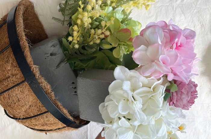 Coir-lined hanging basket being filled with grey florist’s foam, faux hydrangeas and greenery.