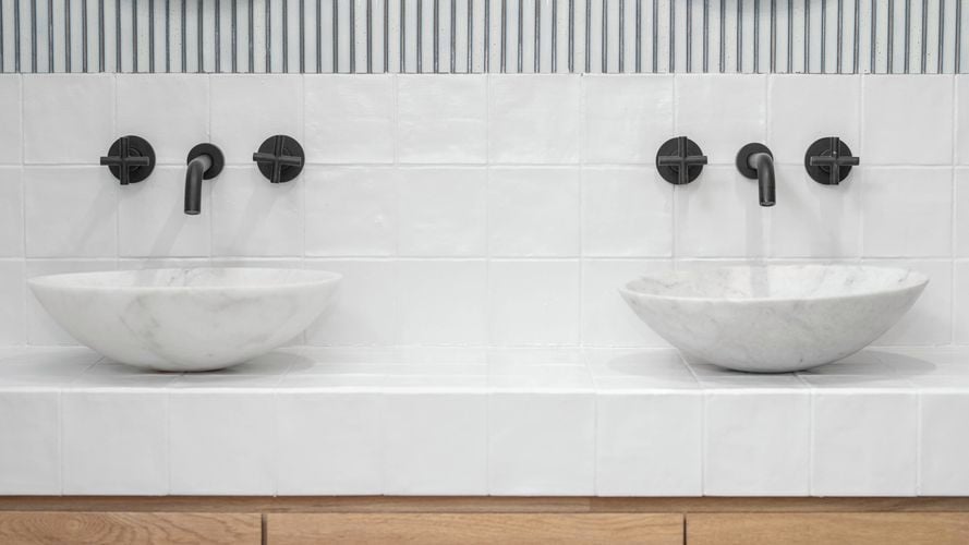 An image of a bathroom with white tiles and black tapware