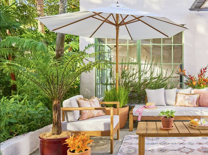 An outdoor patio setting with a raised bed to the left, a table, lounge with stylish cushions and a white and timber market umbrella.