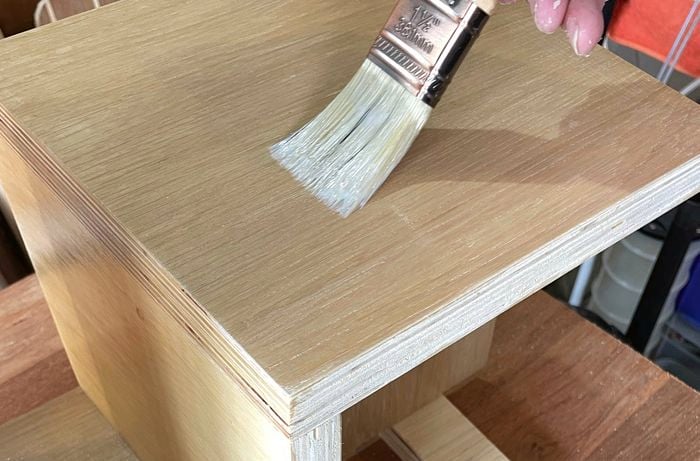 Varnish is applied to the finished table using a paintbrush