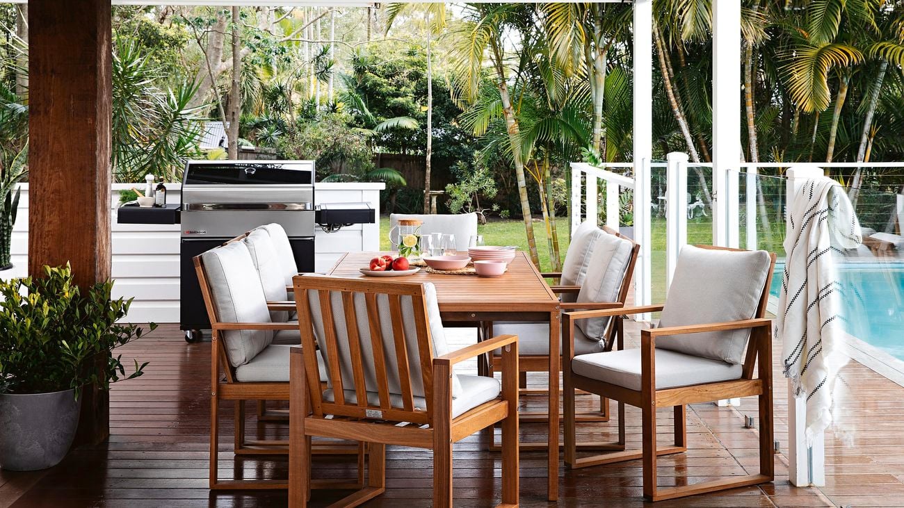 A red stained outdoor dining set on a matching red stained deck, with a pool nearby