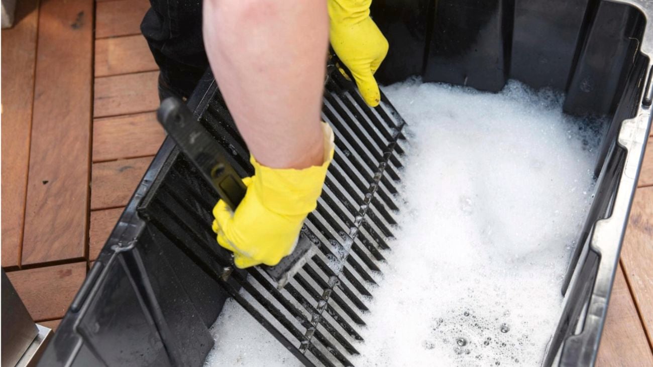 A person wearing gloves scrubbing a barbecue grill in soapy water