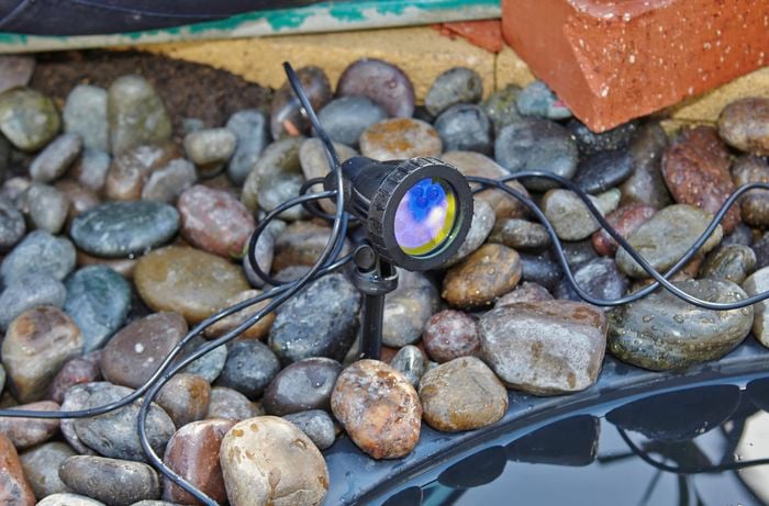 A pond light shining a blue light sitting among pebbles