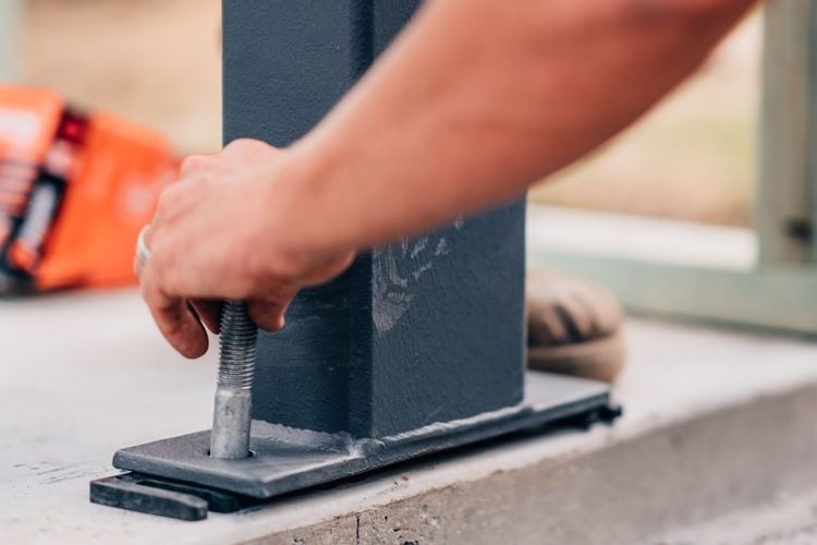 Person inserting a bolt into the foot of a steel post