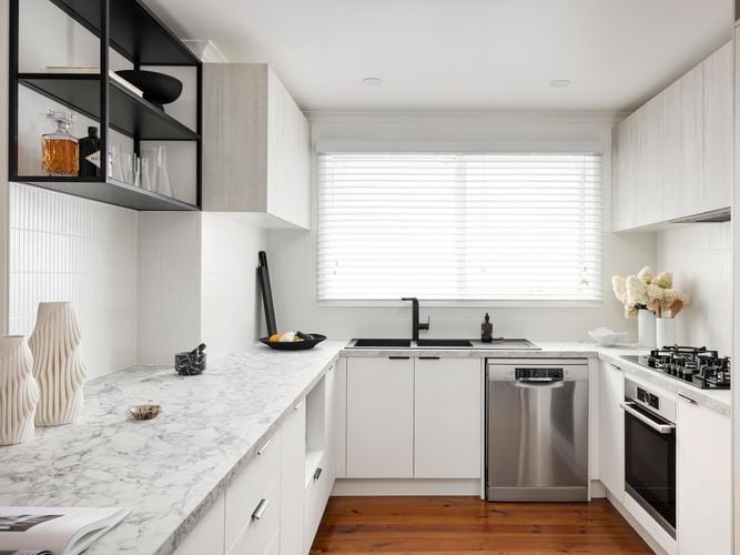 Bright modern white kitchen with venetian blinds, white cabinets and black finishes.