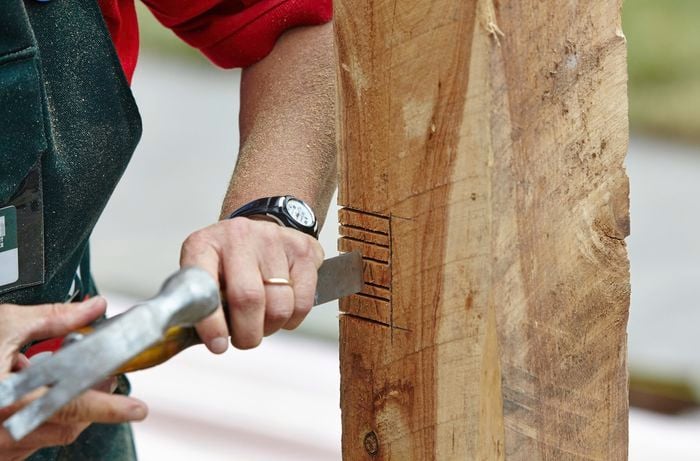 A person using a chisel and hammer to cut out slots in a fence post 
