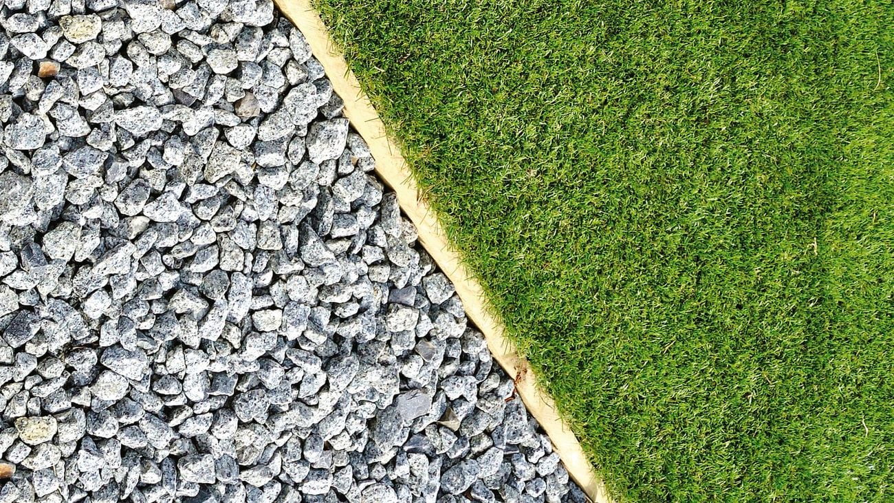 Gravel, pebbles and grass separated by retaining wall.