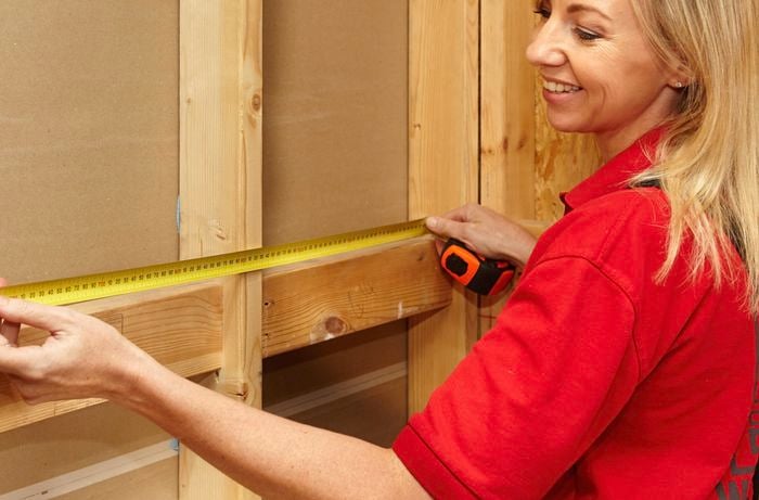 A woman measuring between studs on a wall frame