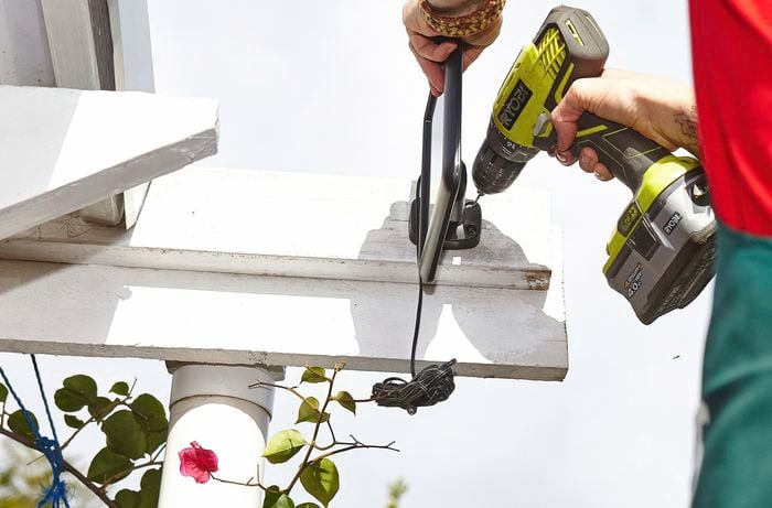 A person drilling a hole in the beam of a pergola to mount a solar panel