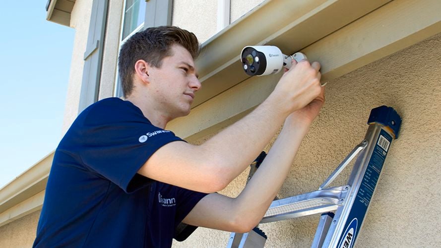 A man installing a security camera to a house exterior