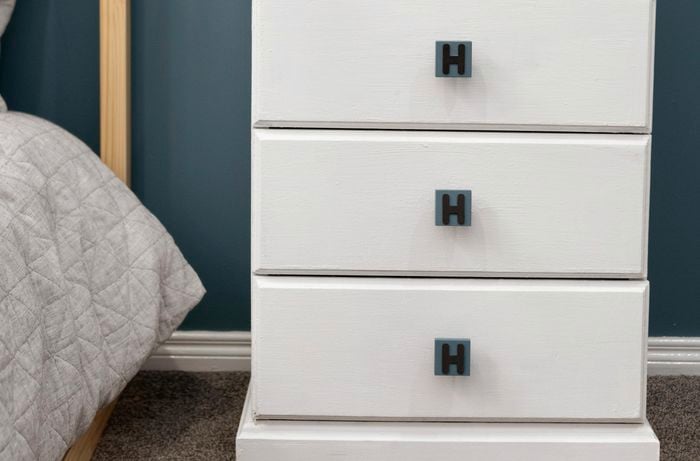 A white chest of drawers with handles customised with the letter H, in a blue themed bedroom setting