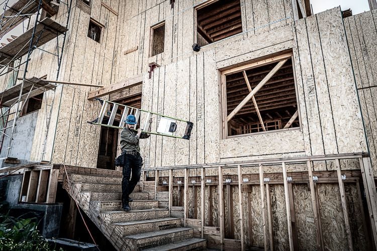 Man wearing a hard hat carrying a light folded up ladder over his shoulder