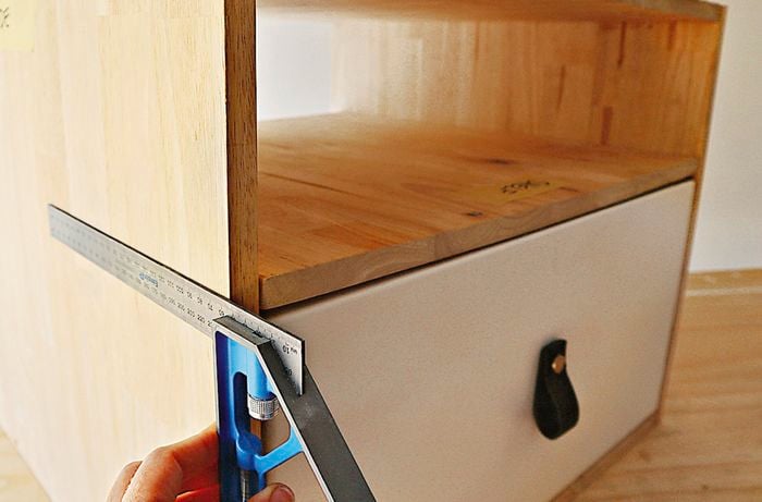 A person measures the shelf above the drawer cabinet