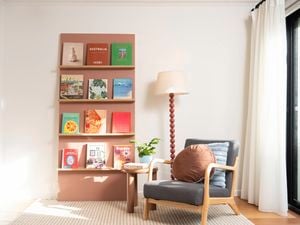 DIY bookshelf made from painted wall panels with timber ledges, styled with books, a floor lamp and armchair.