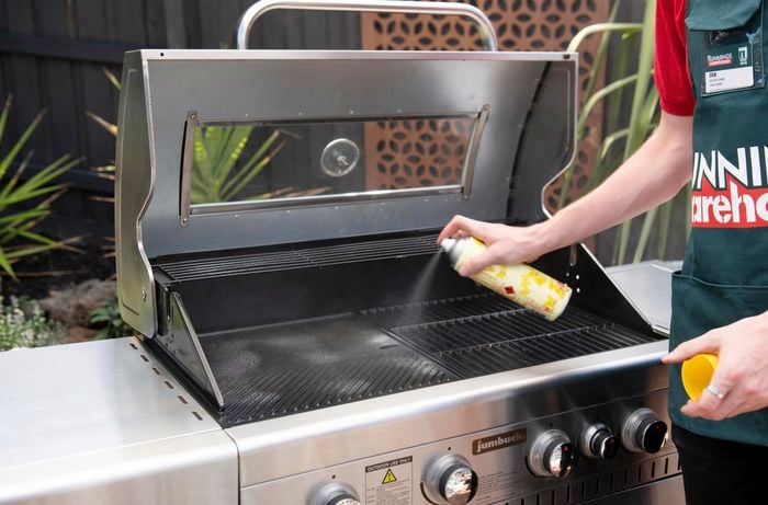 A person spraying BBQ grill plates with cooking oil 