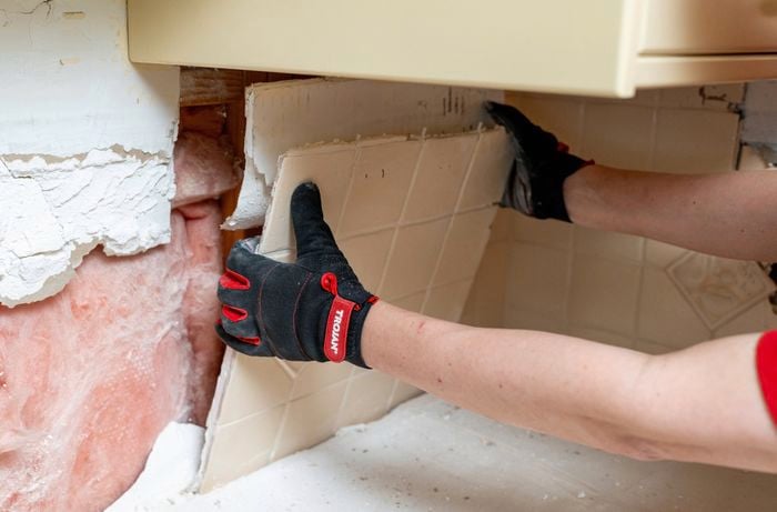 A person is removing cut sections of damaged plasterboard from wall