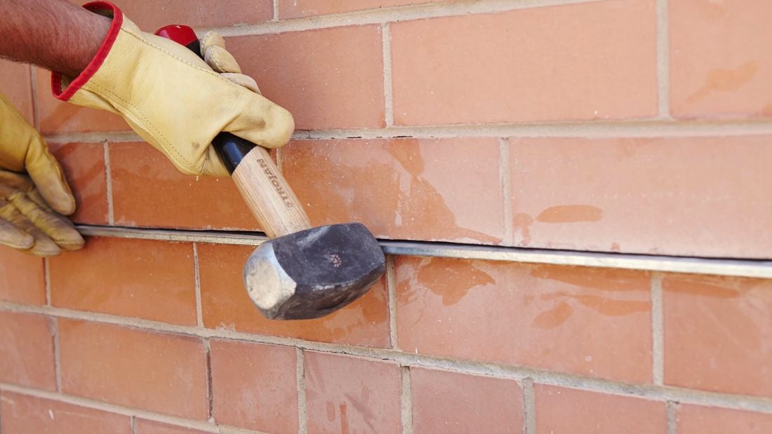 A person using a rubber mallet to insert a metal lintel into a slot in brickwork