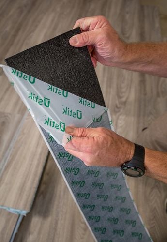 Close up of hands peeling backing off a strip of vinyl plank flooring