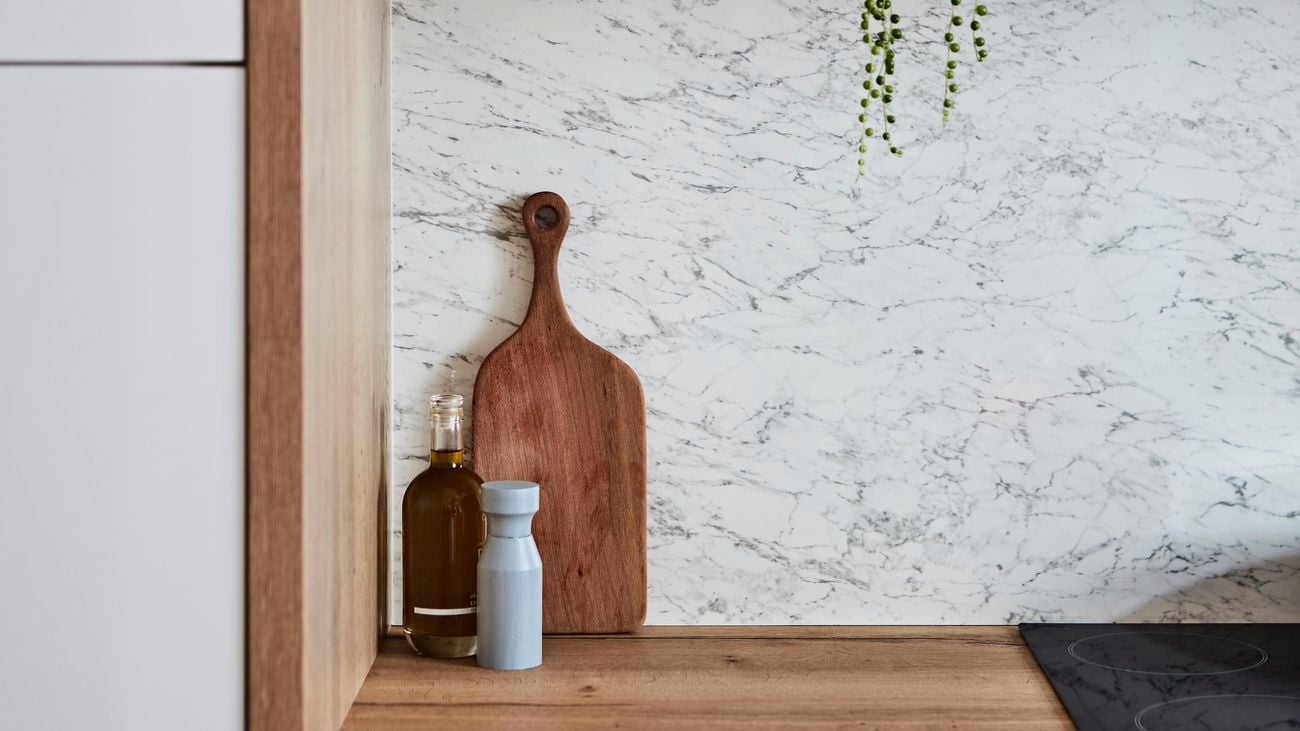 Bottle of oil, salt shaker and wooden serving platter sitting on top of wooden benchtop.