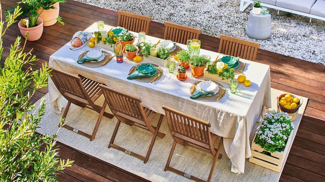An outdoor timber dining setting with a decorated table laden with herb pots, place settings and lemons showcasing biophilic design.