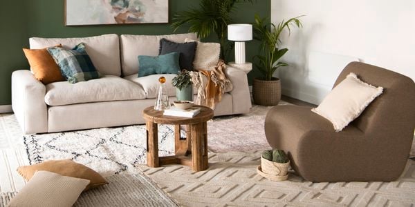 Layered interior rugs in a living room featuring a calming green feature wall and warm brown toned furniture.