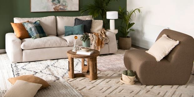 Layered interior rugs in a living room featuring a calming green feature wall and warm brown toned furniture.