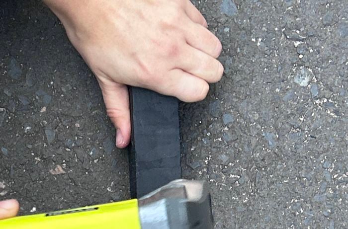A hand holds a nail as it is hammered into a black hardwood garden stake