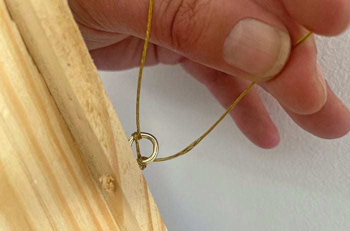 Close up image of a hand holding twine that’s attached to a screw eye on a wooden picture frame to make a gallery wall