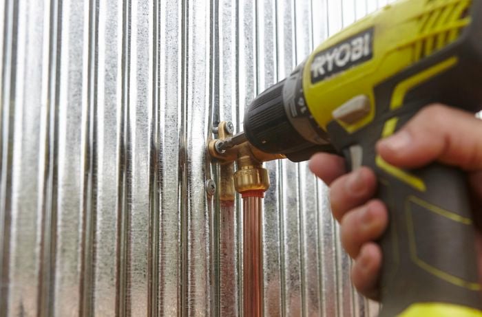 Person securing copper pipe to metal wall.
