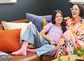 Happy pair lounging on tan leather sofa with colourful pillows in a neurodivergent design space featuring contrasting dark walls, varied textures, and vibrant sensory-friendly elements