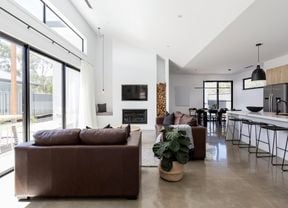 Modern living room with brown leather couches, concrete floors and a fireplace next to a tall stack of wood logs.