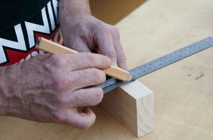 Person measuring bit of timber with steel ruler.