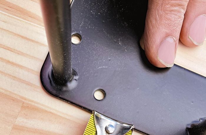 A person measures, positions and secures hairpin legs to a dining table