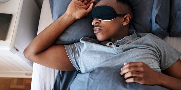 A man sleeping in bed with an eye mask on.