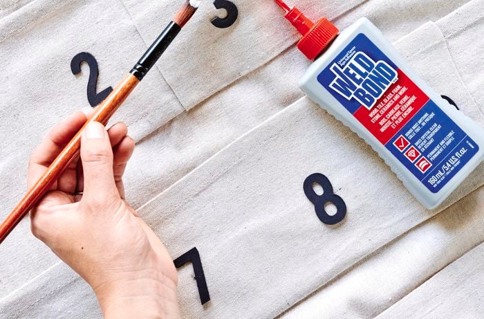 A person uses glue to attach craft numbers to a drop sheet DIY project
